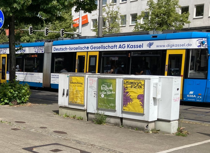 Tram with German-Israel friendship banner with in foreground documenta fifteen poster in Germany's Kassel